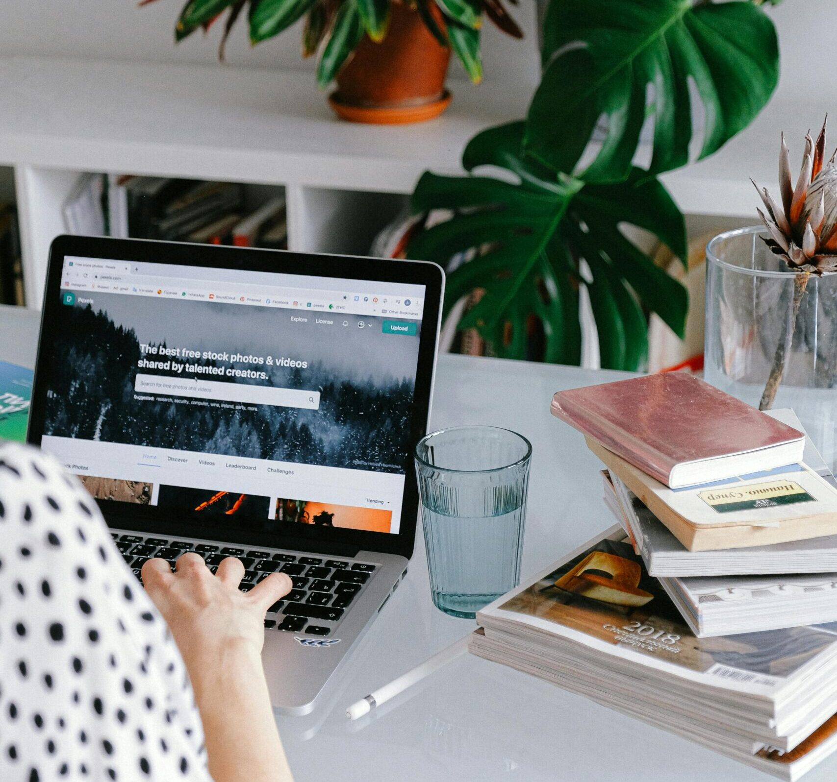 A woman working from home on her laptop surrounded by plants and books for a cozy office feel.