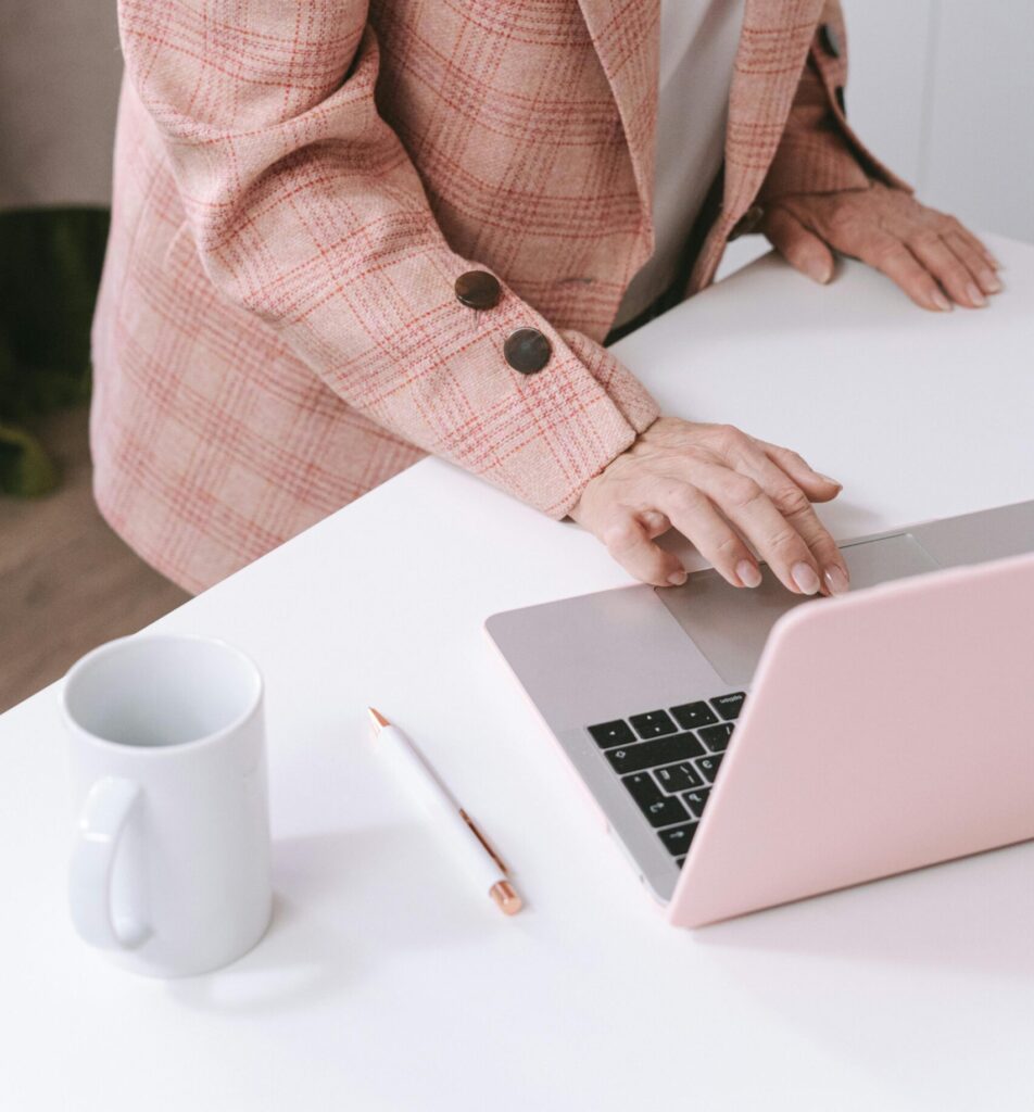 Businesswoman in a pink plaid suit using a laptop at a desk with a coffee mug.